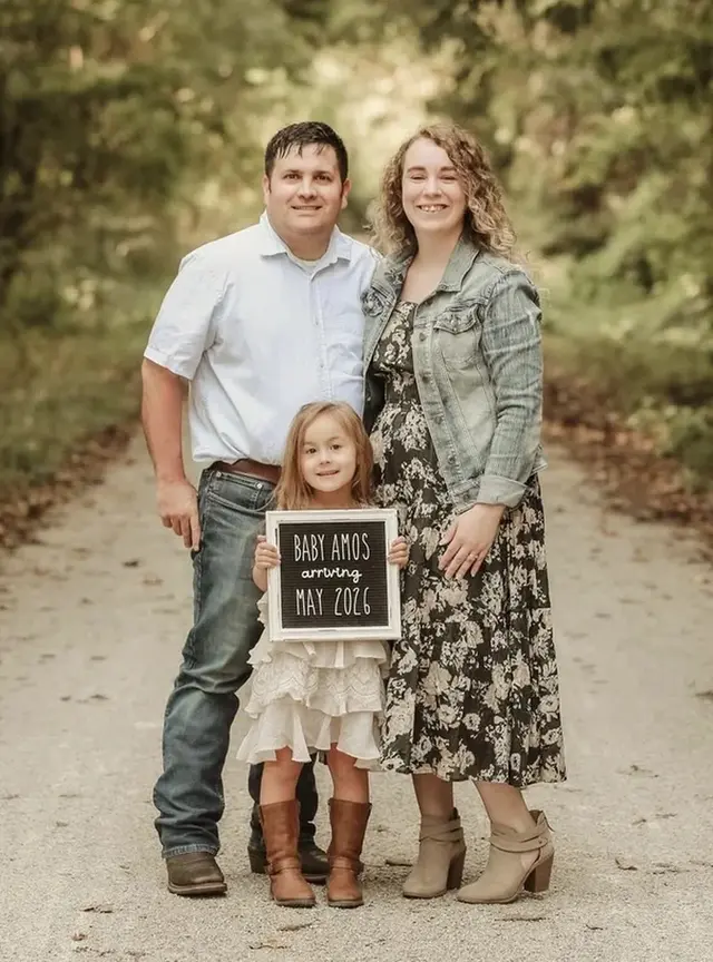 Alicia A. with her husband and daughter, holding a sign announcing their baby, Arbor Fertility patients