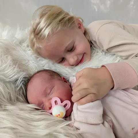 Jess H.'s two daughters: a big sister cuddling her newborn sister, Arbor Fertility patients
